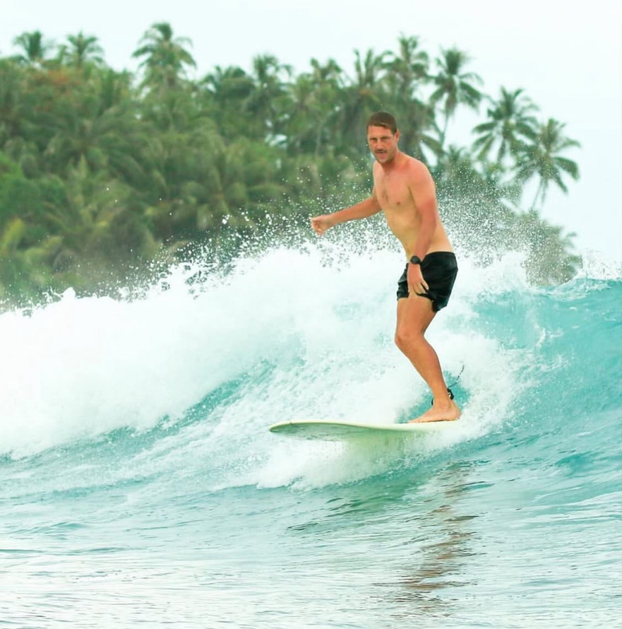 Rory surfing a clean wave in front of palms
